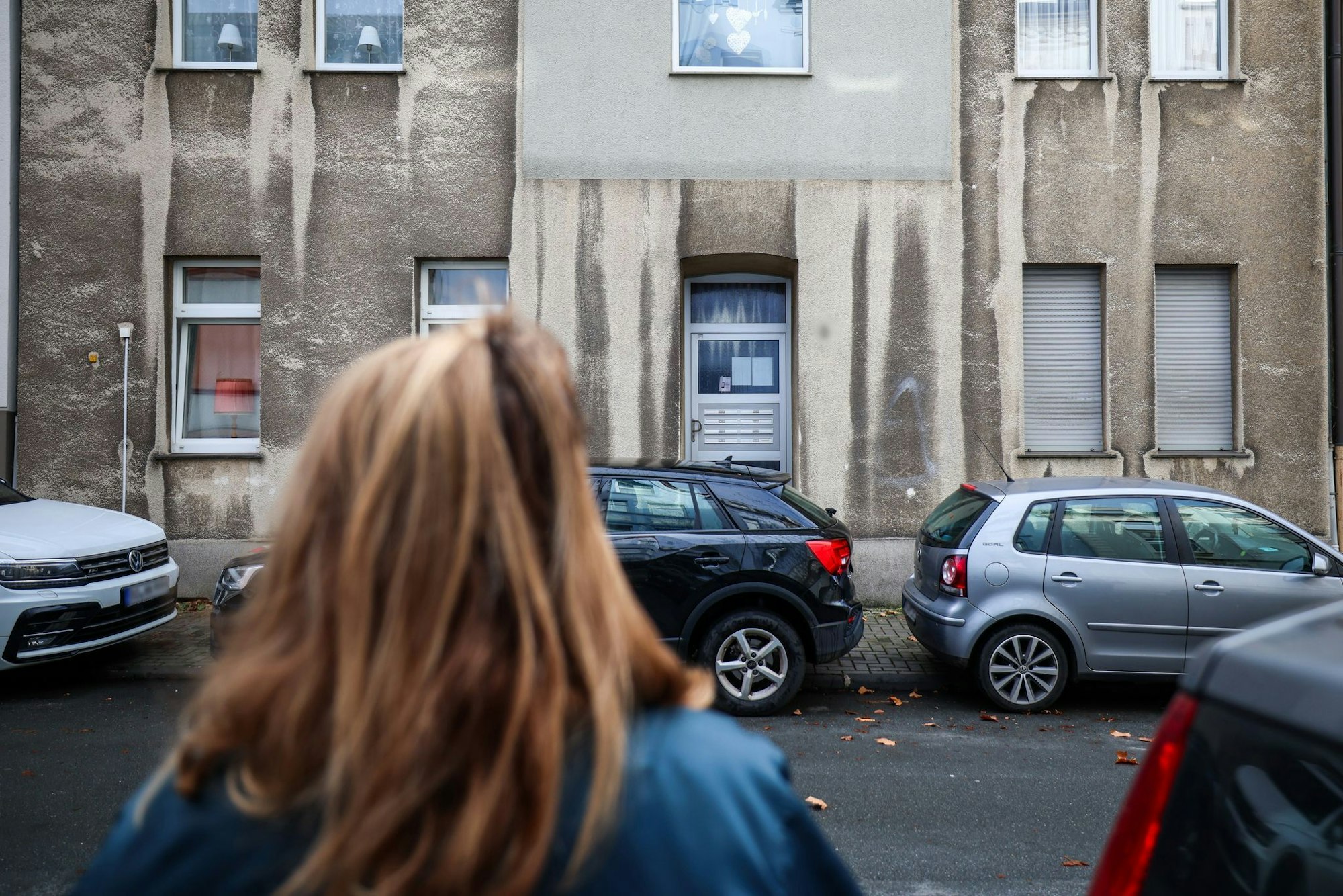 Eine Frau steht vor dem Mehrfamilienhaus, in dem ein zwölfjähriges Mädchen bei einem Polizeieinsatz durch Schüsse lebensgefährlich verletzt worden.