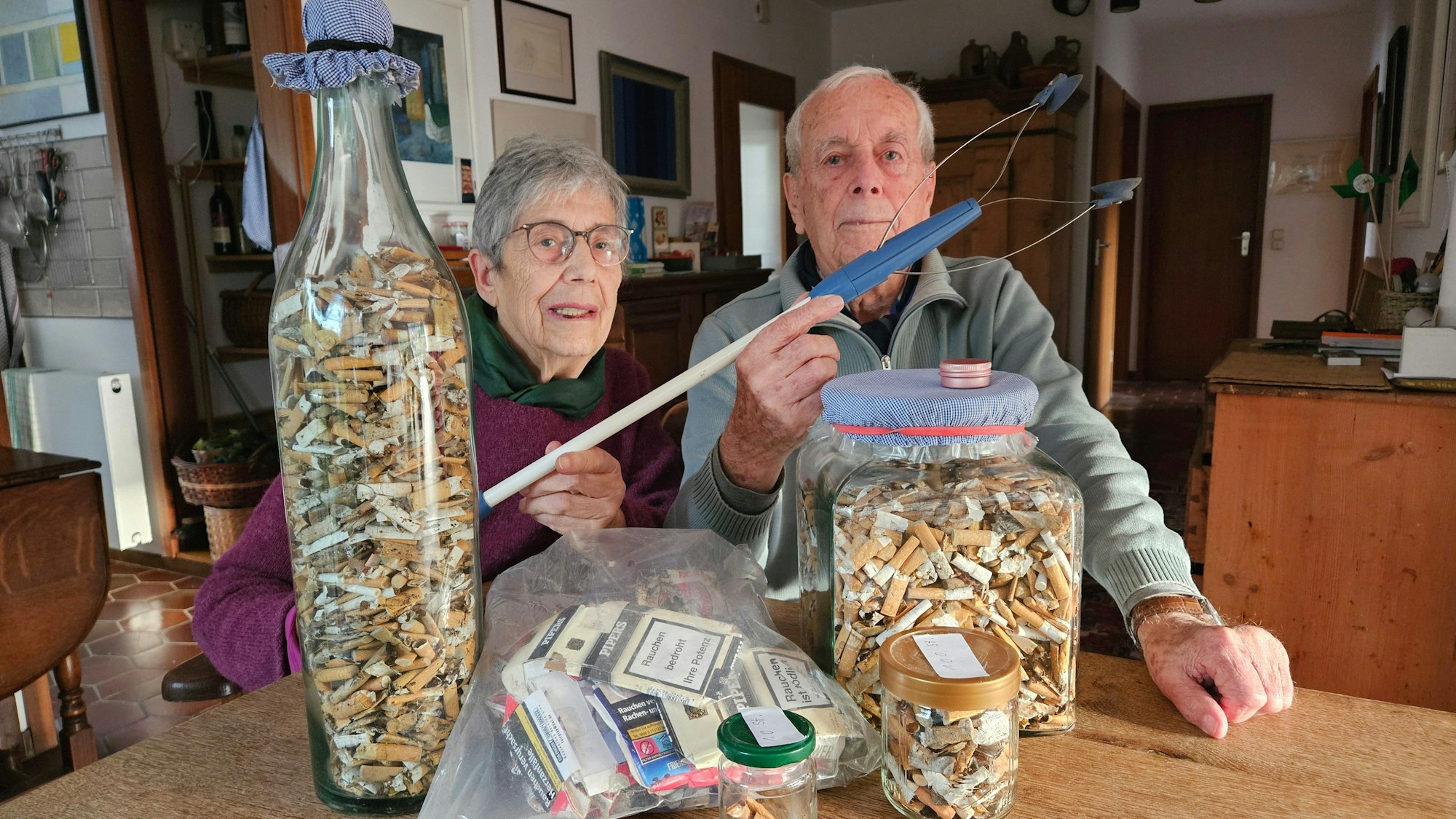 Das Foto zeigt das Ehepaar Margret und Wolfgang Rieve sowie zahlreiche Zigarettenkippen in großen Glasbehältern.