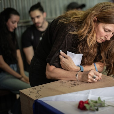 Das Bild zeigt Ricarda Louk, wie sie auf der Beerdigung auf den mit einer Flagge bedeckten Sarg ihrer Tochter Shani Louk schreibt. Die 22-jährige Shani Louk wurde auf der Flucht von einem Musikfestival während des Hamas-Angriffs am 7. Oktober 2023 getötet worden.