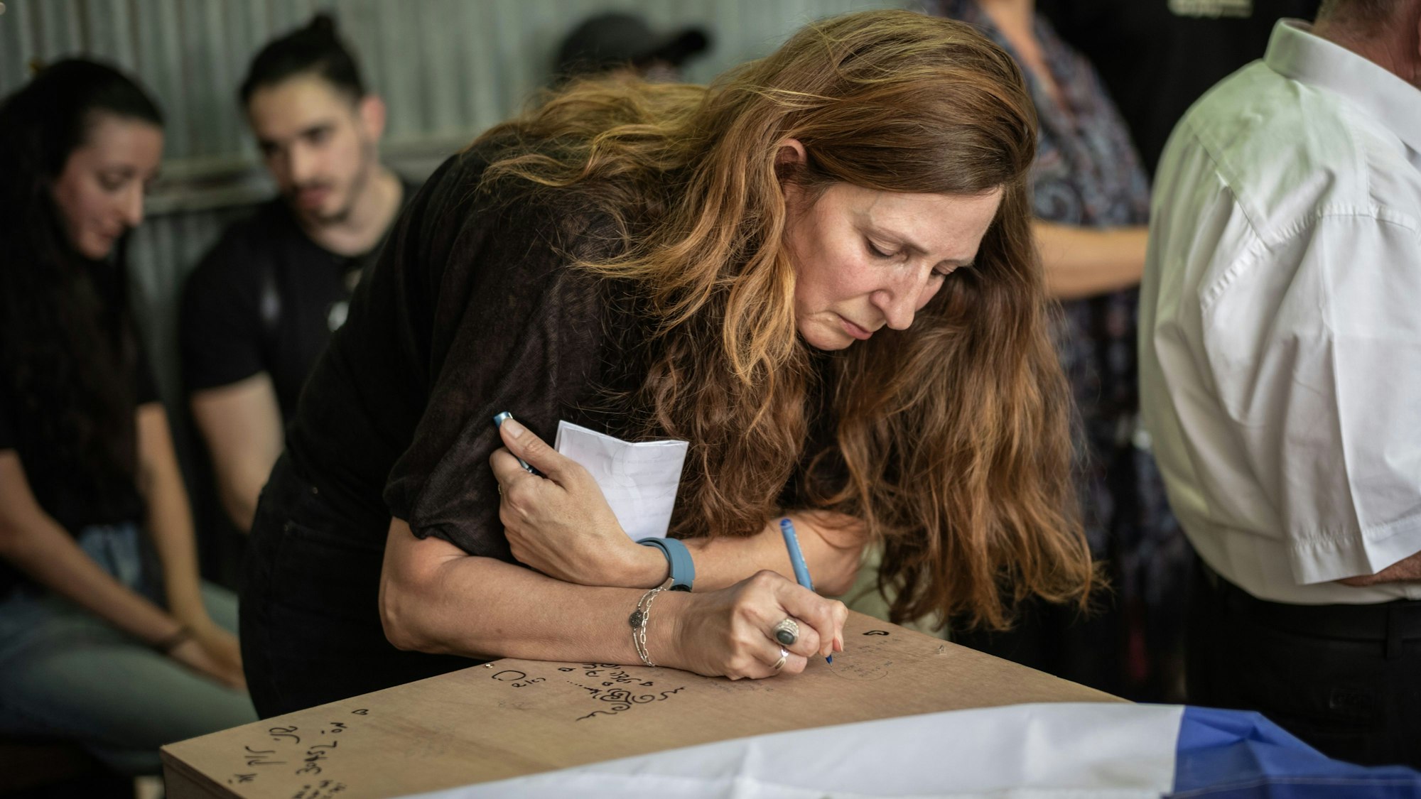 Das Bild zeigt Ricarda Louk, wie sie auf der Beerdigung auf den mit einer Flagge bedeckten Sarg ihrer Tochter Shani Louk schreibt. Die 22-jährige Shani Louk wurde auf der Flucht von einem Musikfestival während des Hamas-Angriffs am 7. Oktober 2023 getötet worden.