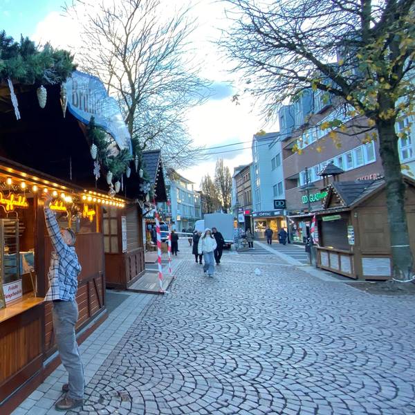 Zu sehen ist einer der Stände des Weihnachtsmarktes. Zwei Mitarbeiter sind mit dem Aufbauen beschäftigt.