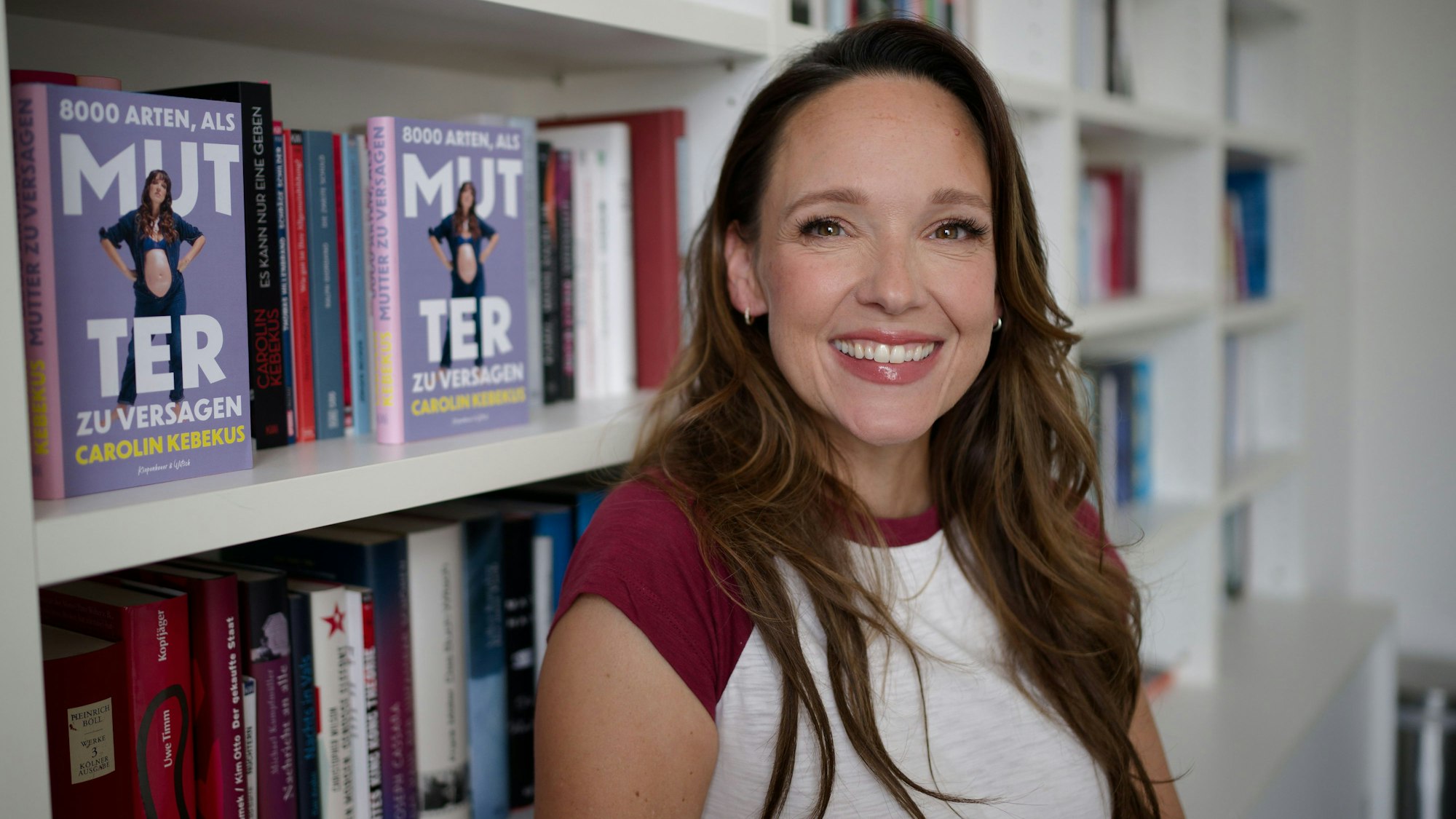 Comedian und Autorin Carolin Kebekus steht an einem Bücherregal.