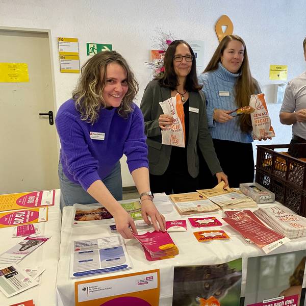 Zwei Mitarbeiterinnen der Frauenberatungsstelle, die Gleichstellungsbeauftragte und der Bürgermeister stehen hinter dem Infostand, an dem es Broschüren und Flyer gibt sowie Weckbrötchen, die in die speziellen Tüten gepackt werden.