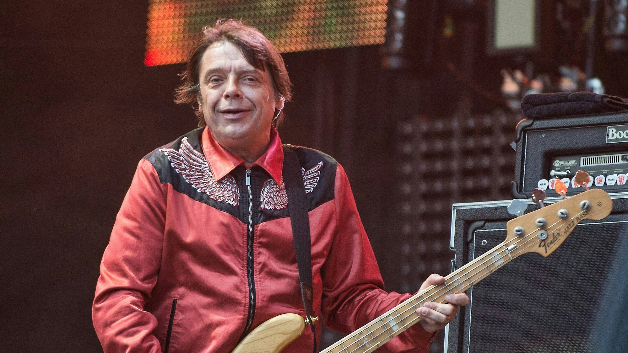 Mani von The Stone Roses spielt Bassgitarre auf der Bühne, trägt eine rote Jacke