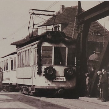 Historische Schwarz-Weiß-Aufnahme einer mit Girlande geschmückten Straßenbahn.