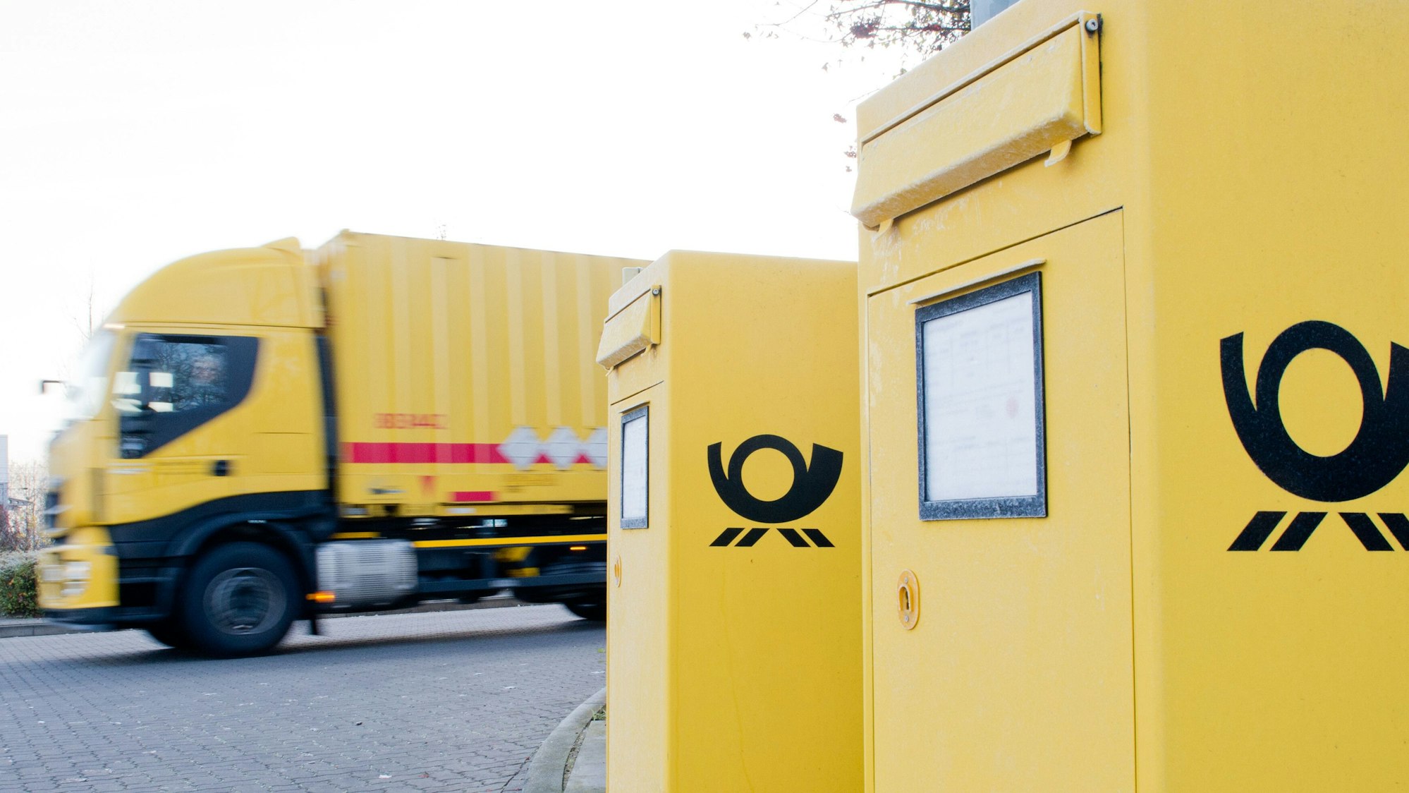 Ein Lkw der Deutschen Post AG verlässt ein Paketzentrum, davor sind zwei Briefkästen zu sehen.