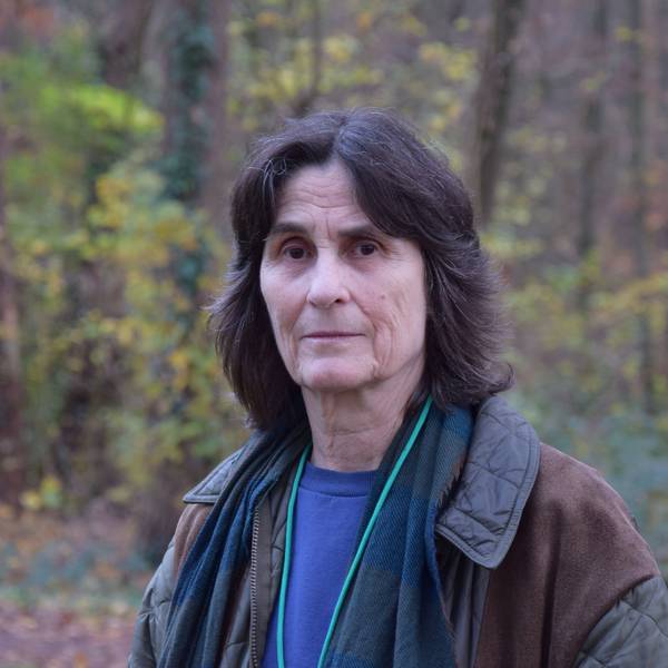 Eine Frau mit schwarzen Haaren steht in einem Waldstück.