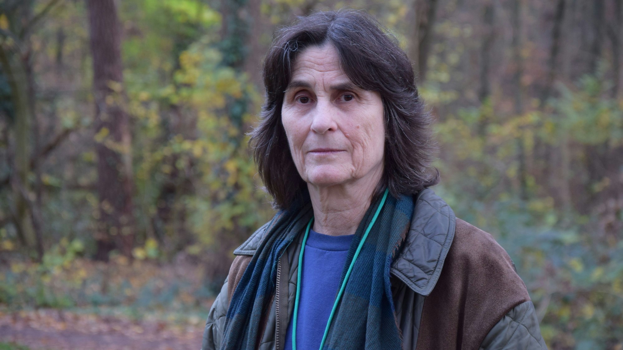 Eine Frau mit schwarzen Haaren steht in einem Waldstück.