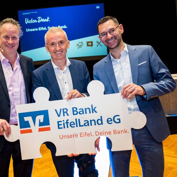 Drei Männer halten ein als Puzzleteile gestaltetes Plakat mit der Aufschrift VR Bank EifelLand eG.