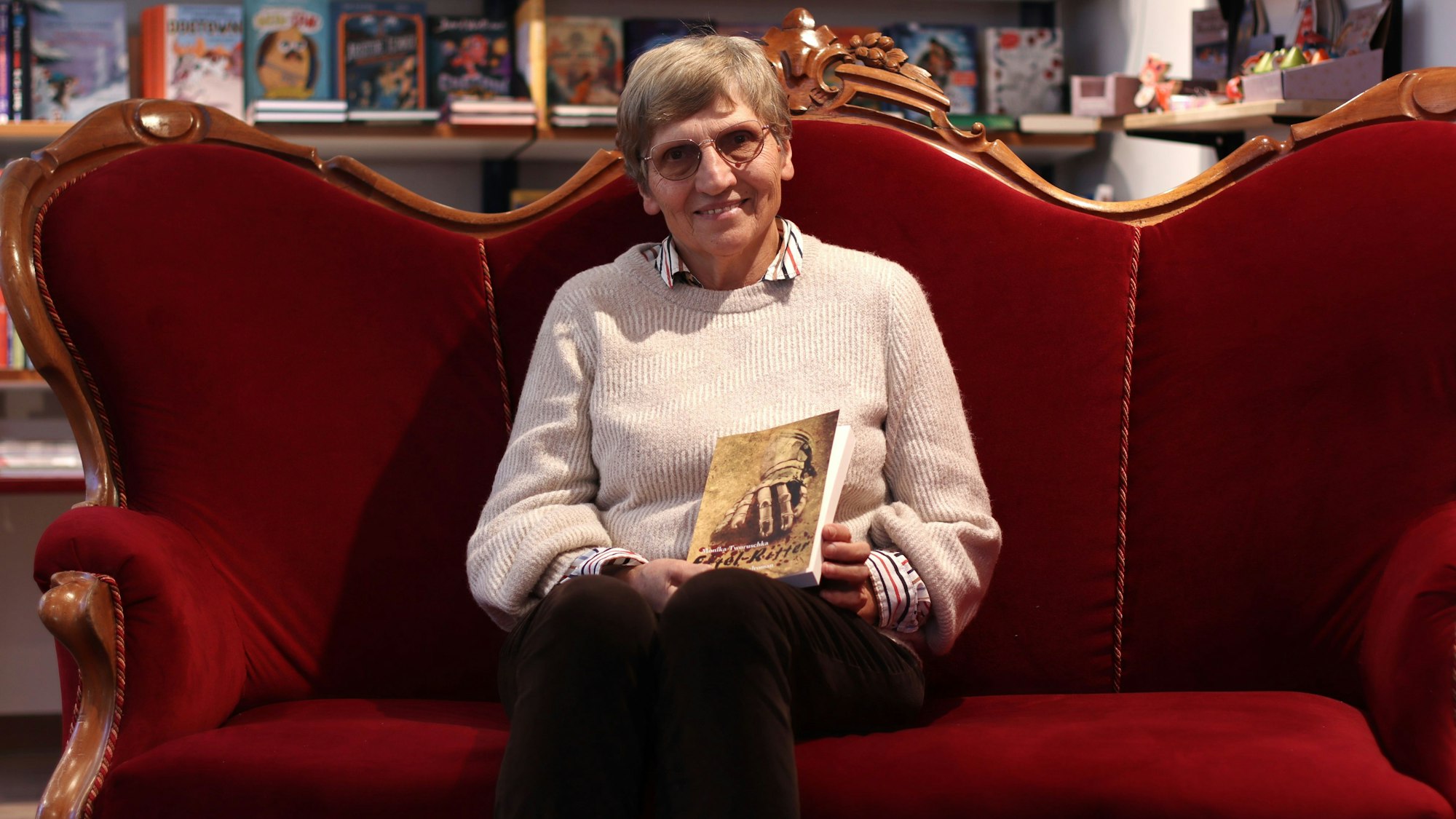 Monika Tworuschka hat auf dem roten Sofa in der Buchhandlung Mütters Platz genommen und hält ihren Roman„ Eifel-Ritter“ in den Händen.