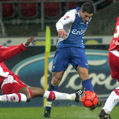 Das Foto zeigt einen Fußballer im blauen Dress, der von seinem Kölner Gegenspieler spektakulär abgegrätscht wird.