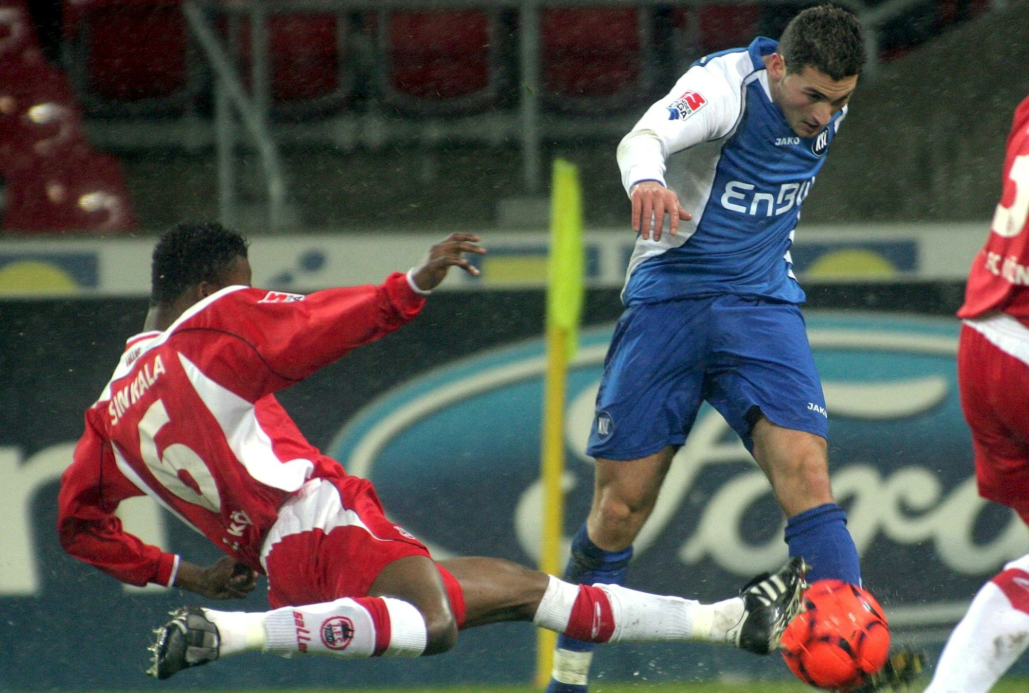 Das Foto zeigt einen Fußballer im blauen Dress, der von seinem Kölner Gegenspieler spektakulär abgegrätscht wird.