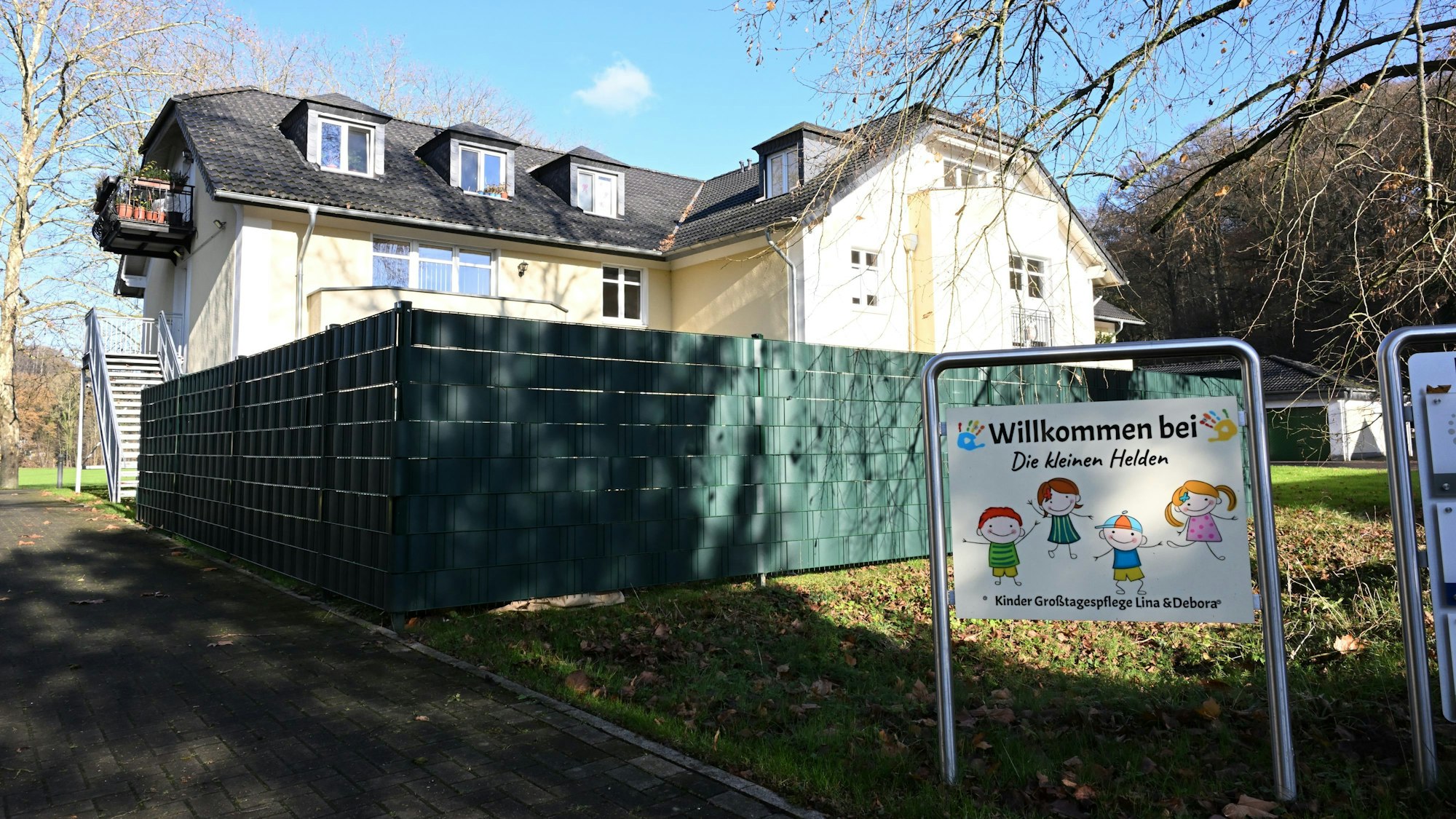 Ein Haus mit Zaun, davor ein Schild, das auf die Großtagespflege „Die kleinen Helden“ hinweist.