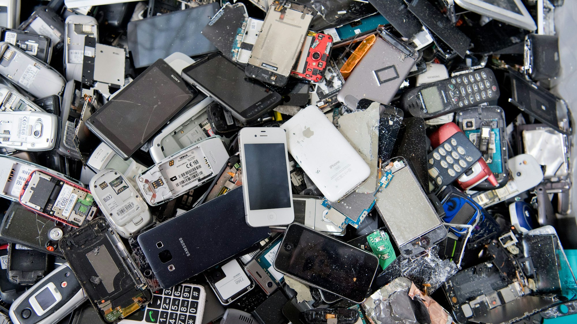 Alte Handys und Smartphones liegen in einem Container.