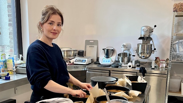 Eine Frau steht in einer Backstube. Auf einem Arbeitstisch stehen verschiedene gefüllte Teigformen.