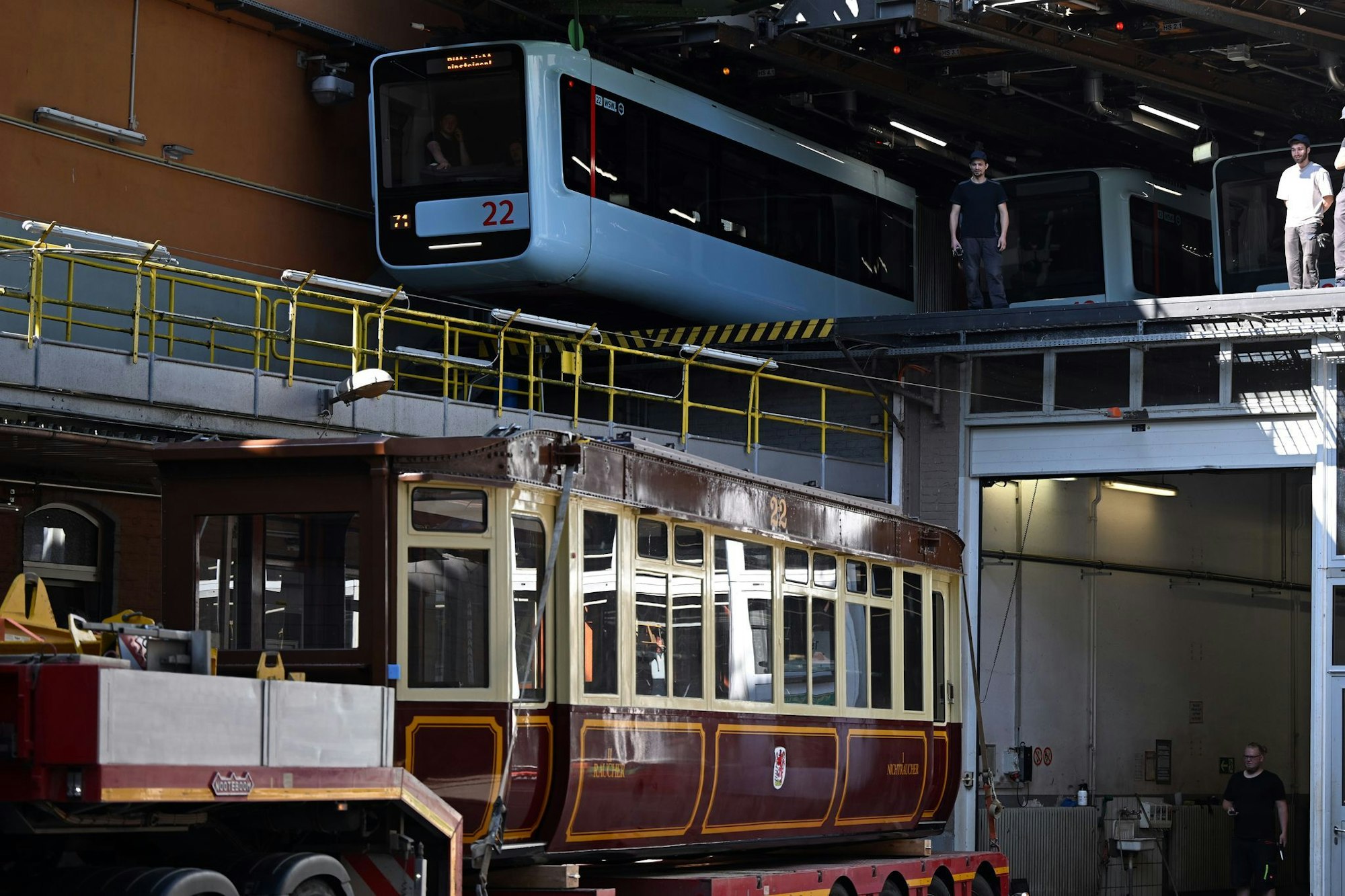 Die Schwebebahn gestern und heute. Ein Wagen der ersten Baureihe 1900 steht auf einem Tieflader unter einem Wagen der aktuellen Baureihe in der Werkstatt der Schwebebahn. (Archivbild)