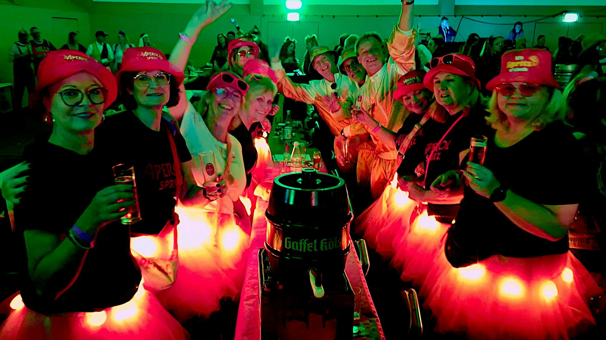 Frauen in Kostümen mit beleuchteten Röckchen feiern an einem Tisch.