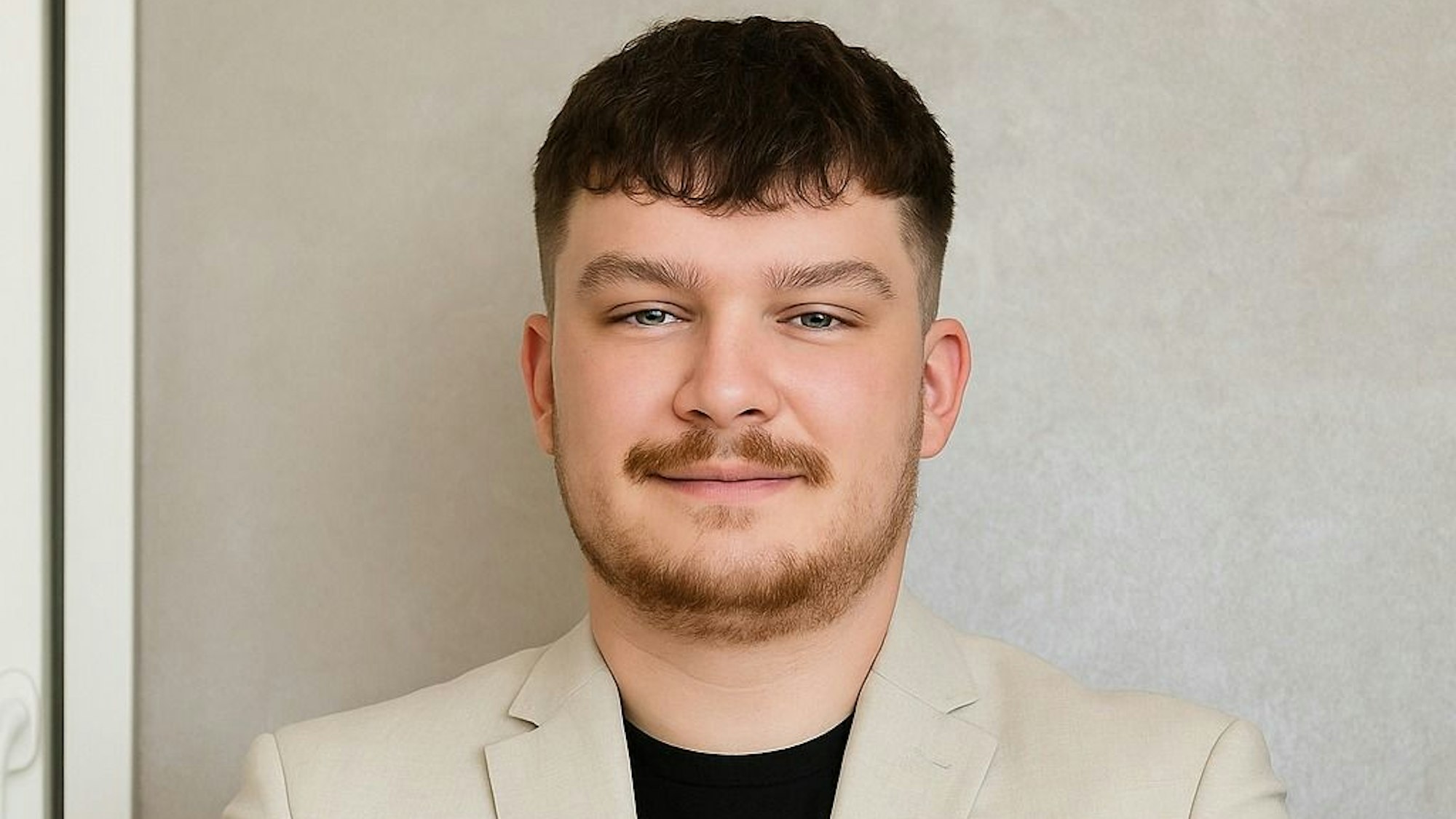 Zu sehen ist ein junger Mann, der vor einer Wand steht.