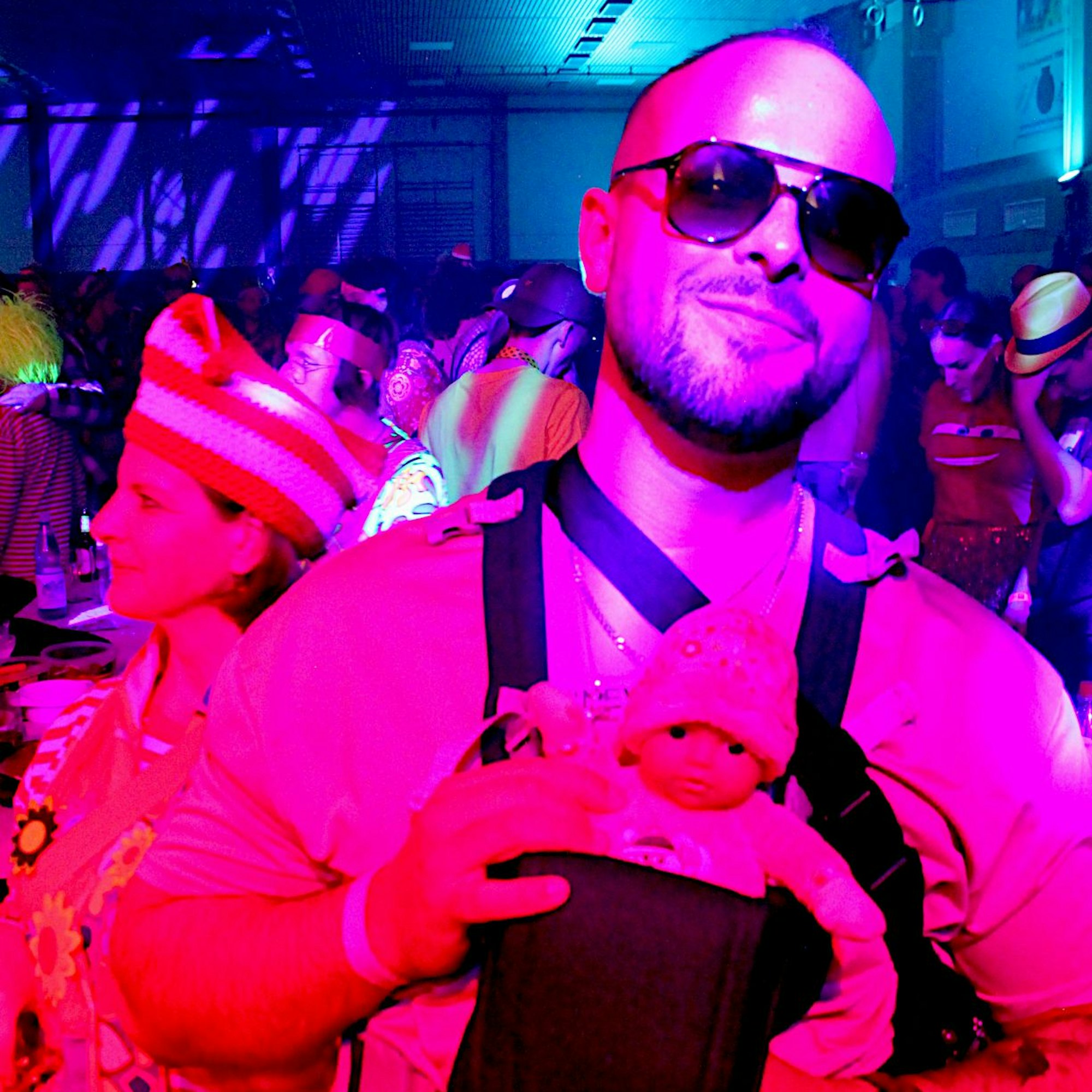 Leon, mit Sonnenbrille, trägt eine kleine Puppe im Rucksack vor der Brust.