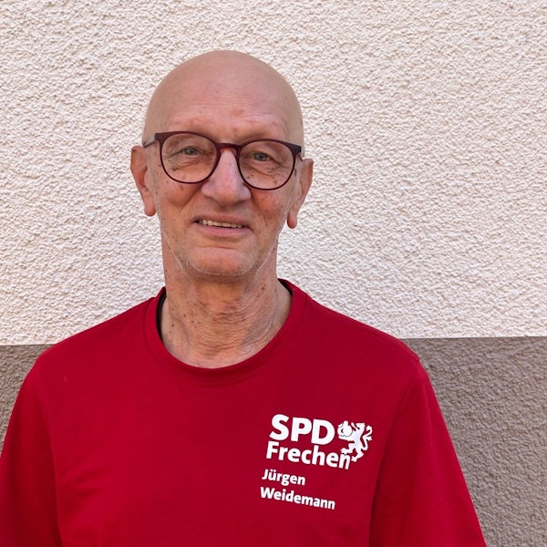 Auf dem Bild ist das Portrait eines Mannes in einem roten T-Shirt vor einer weißen Wand zu sehen.