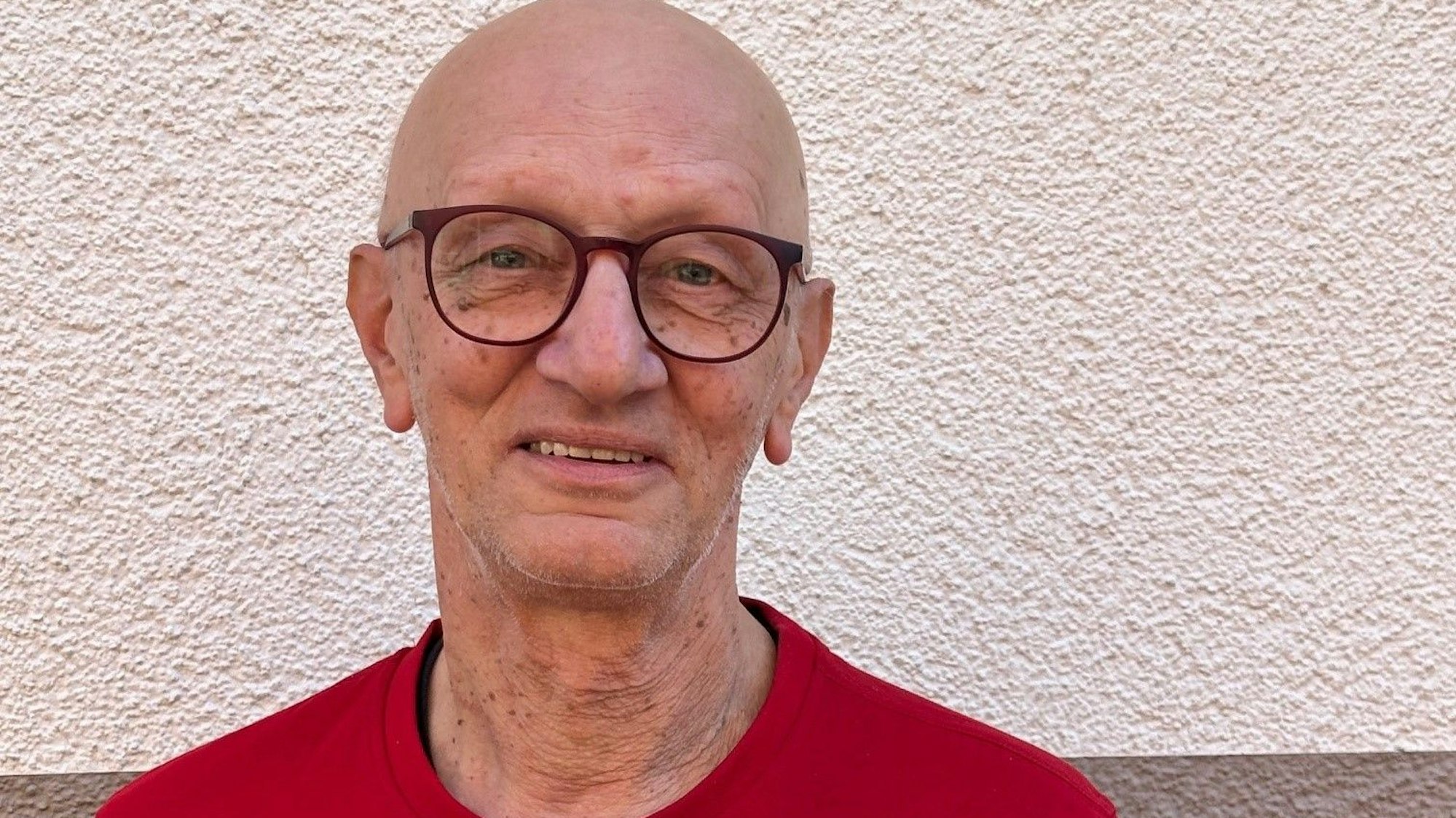 Auf dem Bild ist das Portrait eines Mannes im roten T-Shirt zu sehen.