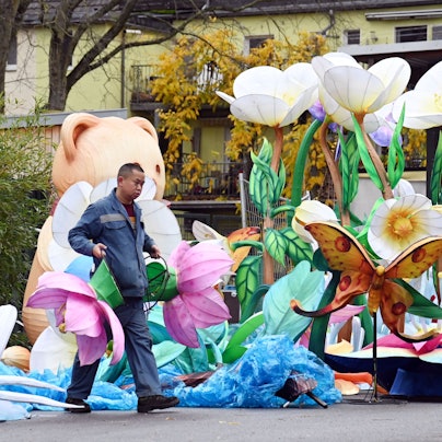 Ein Mann trägt zwei große, pinke Blumen. Ein anderer faltet blauen Stoff zusammen.