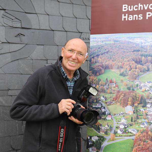 Hans-Peter Barrig hat ein gut 500 Seiten starkes Buch über sein Heimatdorf Käsberg geschrieben. Der Autor vor dem Cover seines Buchs auf einem Roll-up.