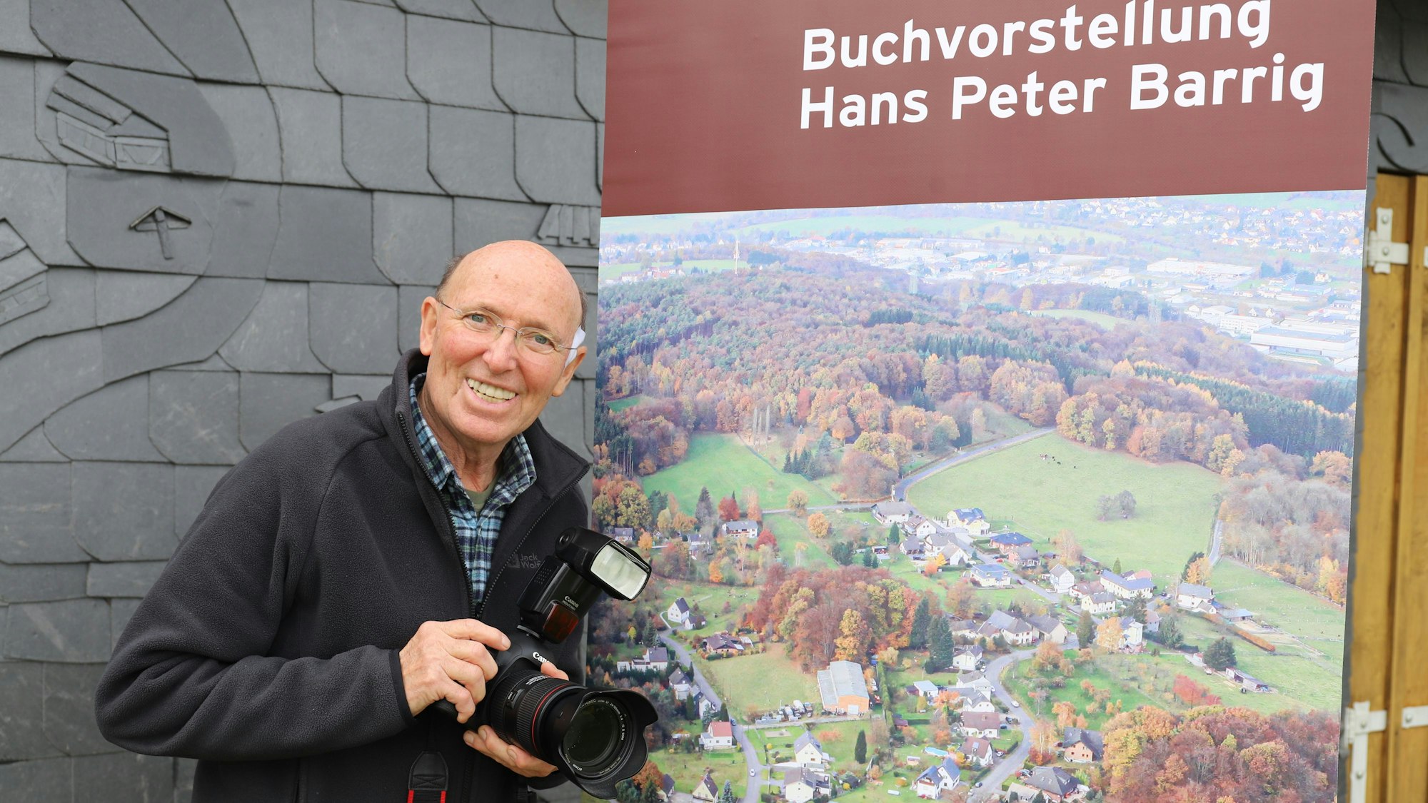 Hans-Peter Barrig hat ein gut 500 Seiten starkes Buch über sein Heimatdorf Käsberg geschrieben. Der Autor vor dem Cover seines Buchs auf einem Roll-up.