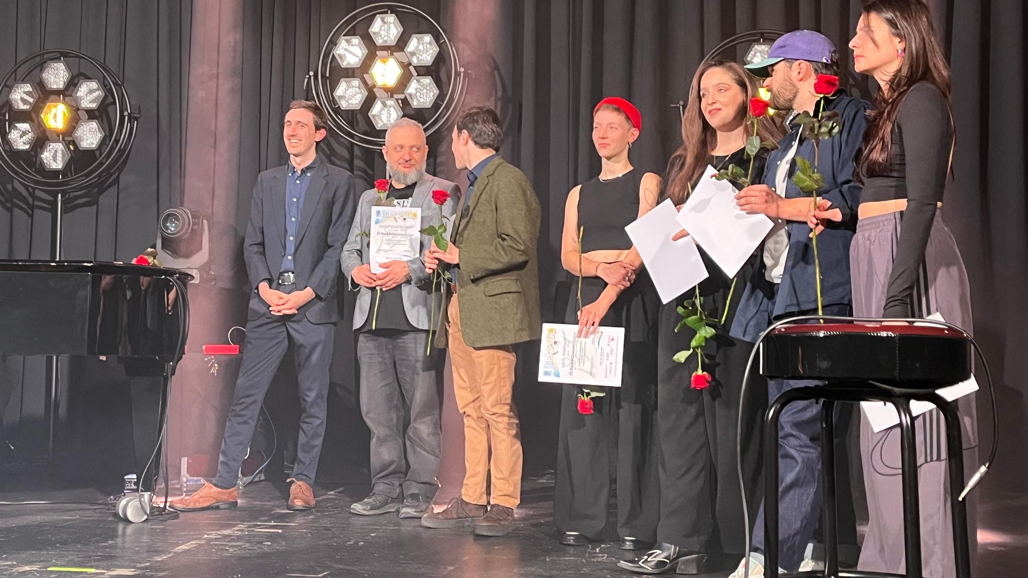 Junge Frauen und Männer stehen mit Rosen in der Hand auf einer Bühne.