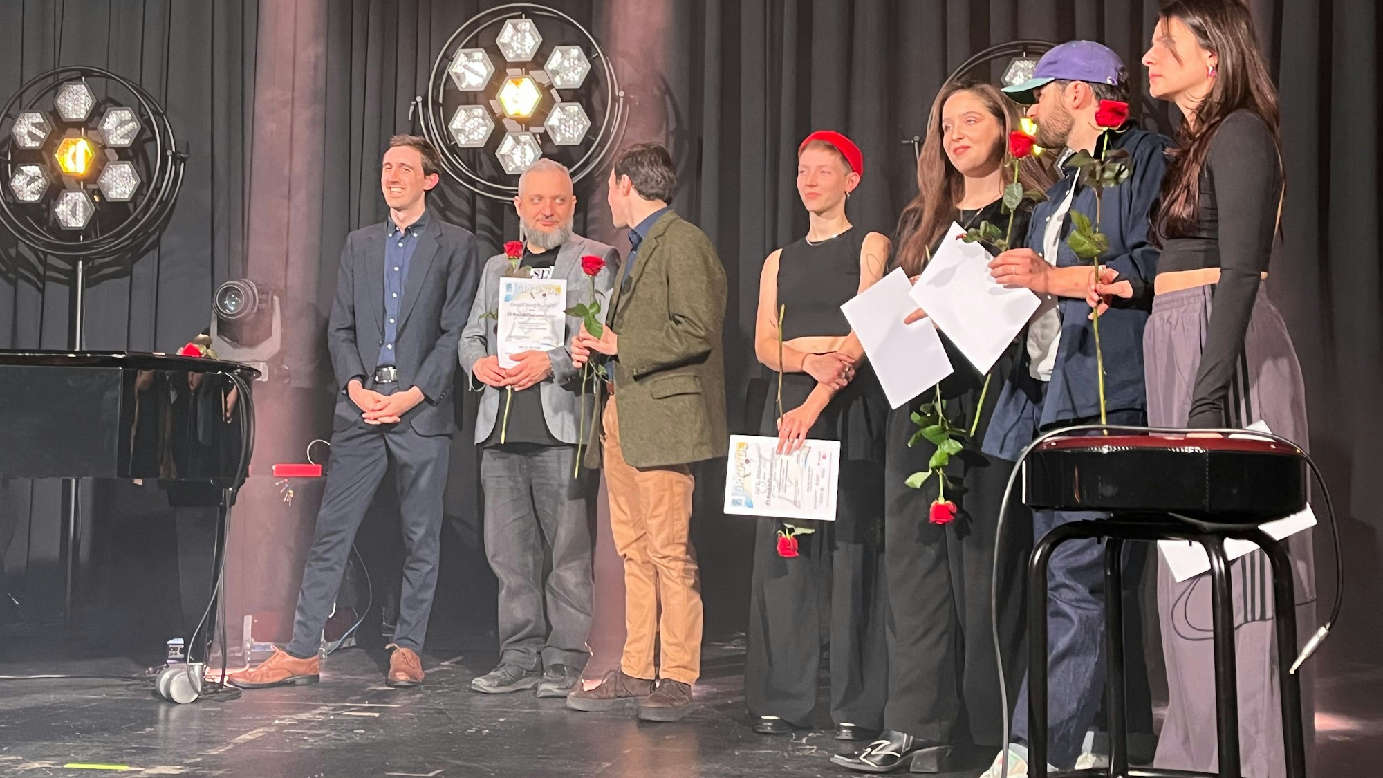 Junge Frauen und Männer stehen mit Rosen in der Hand auf einer Bühne.