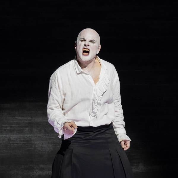 Zu sehen ist ein Schauspieler, der weiße Schminke auf dem Gesicht hat. Er verzerrt das Gesicht schmerzhaft im Gesang. Er trägt ein weißes Shirt und eine schwarze Hose, der Hintergrund ist schwarz.