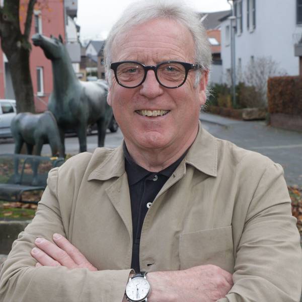 Ein Mann mit weißen Haaren und einer Brille mit schwarzem Gestell lächelt in die Kamera.