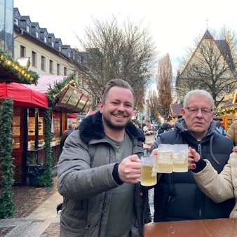 Zu sehen zwei Männer und eine Frau, die sich mit Glühwein zuprosten.