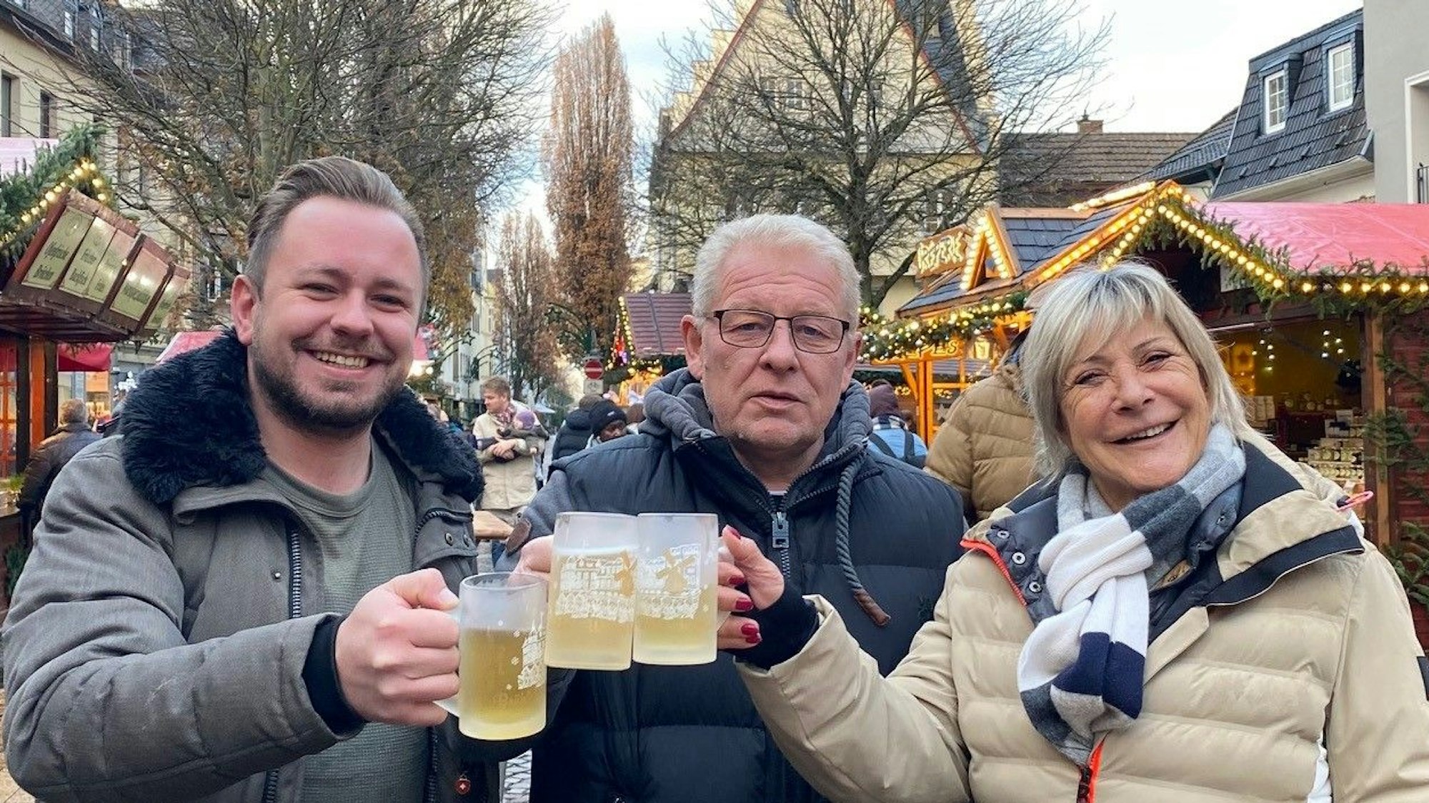 Zu sehen zwei Männer und eine Frau, die sich mit Glühwein zuprosten.