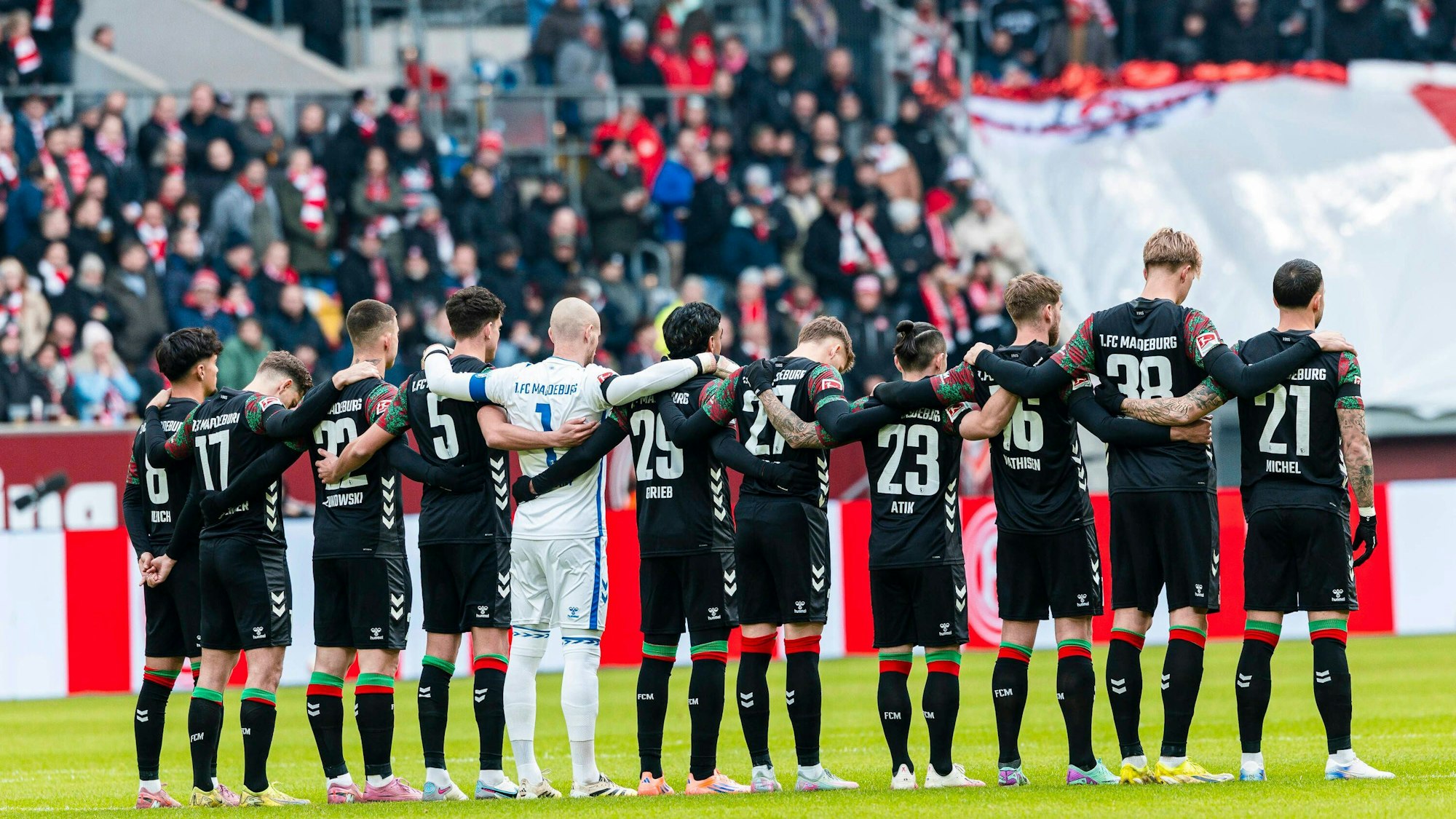 Spieler des 1. FC Magdeburg stehen Arm in Arm vor dem Anpfiff zusammen.