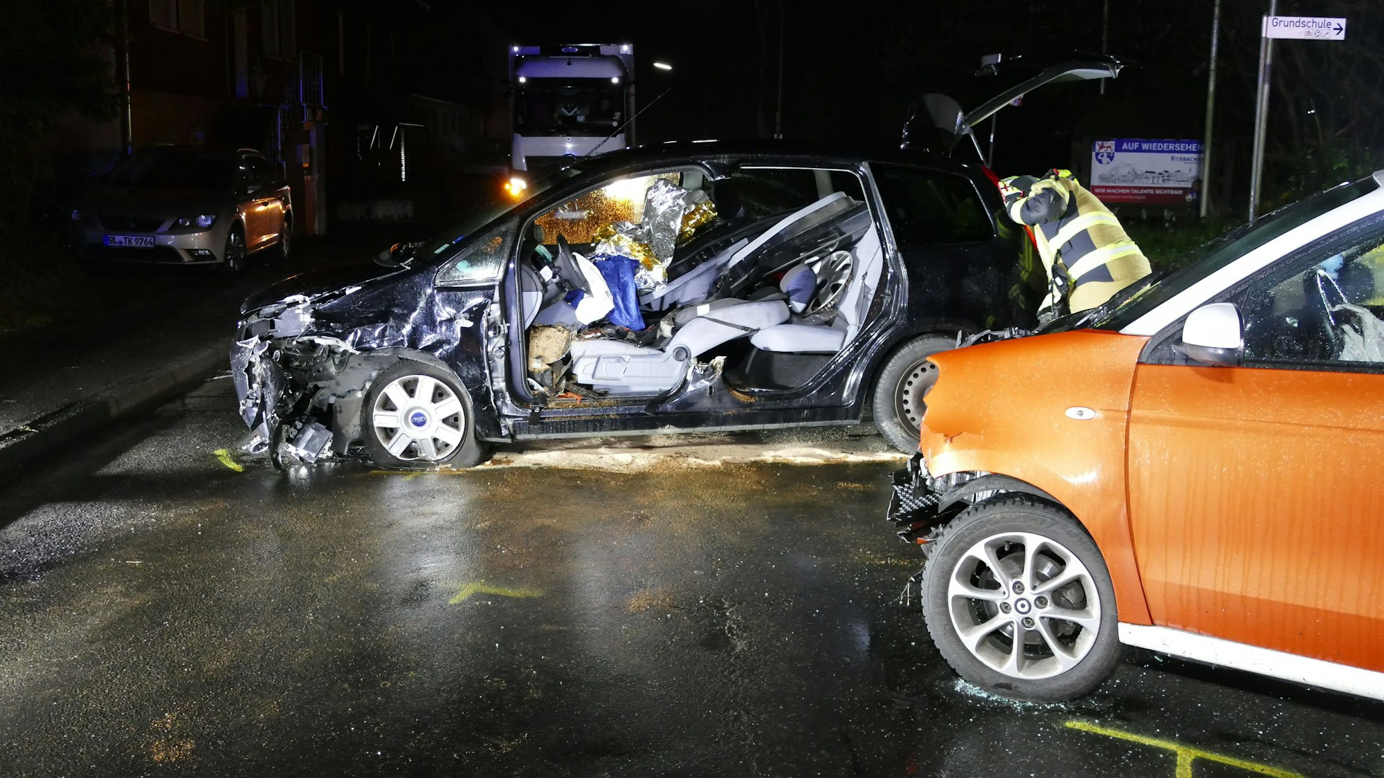 Zwei zerstörte Autos an einer Unfallstelle, es ist dunkel und nass.