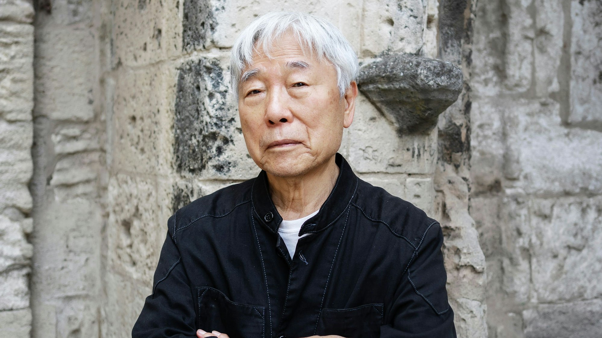 Lee Ufan steht vor einer Mauer.