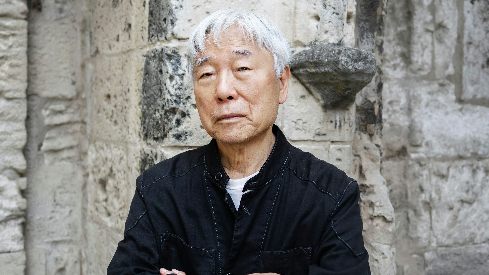 Lee Ufan steht vor einer Mauer.