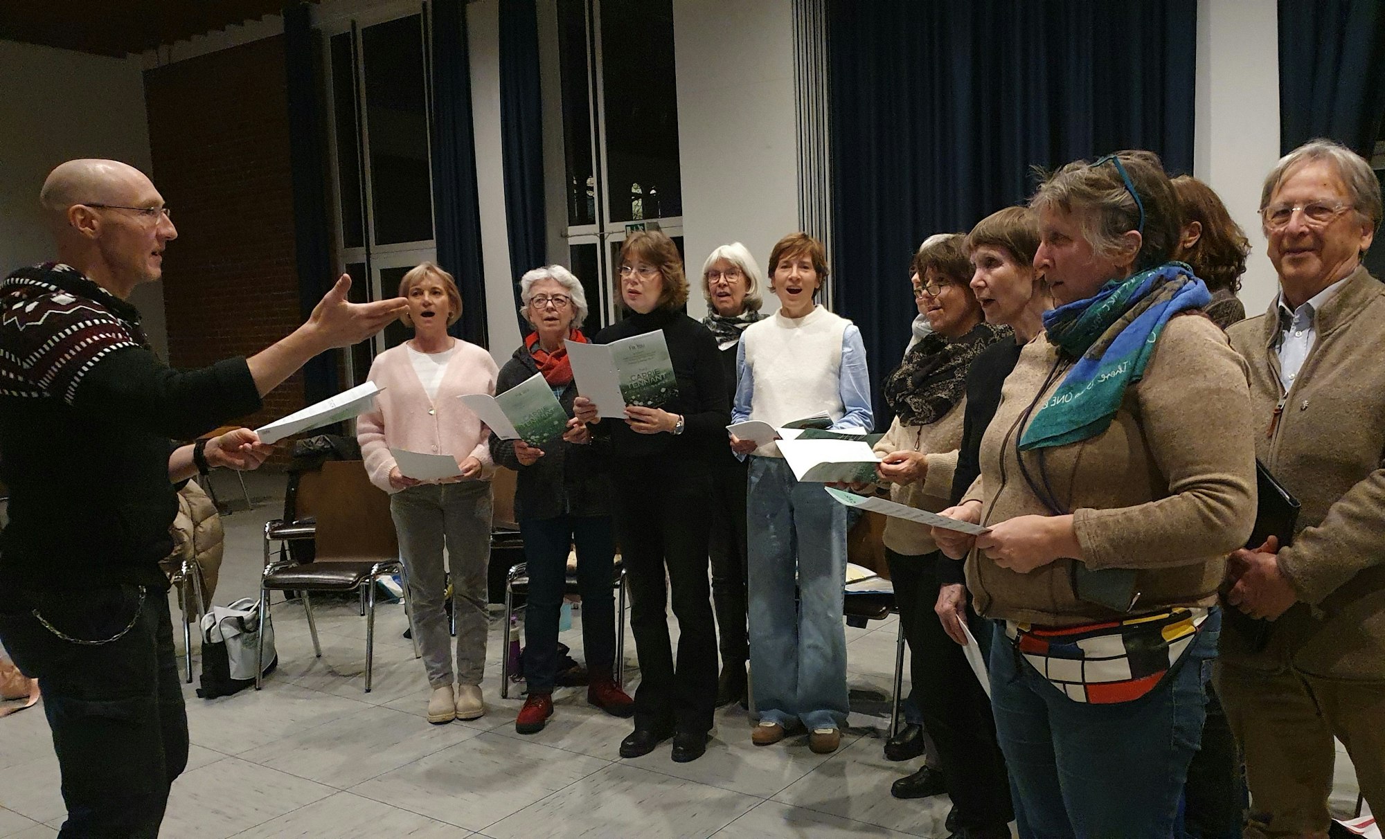 Ein Mann steht vor einer Gruppe Frauen und einem Mann. Er ist der Chorleiter.