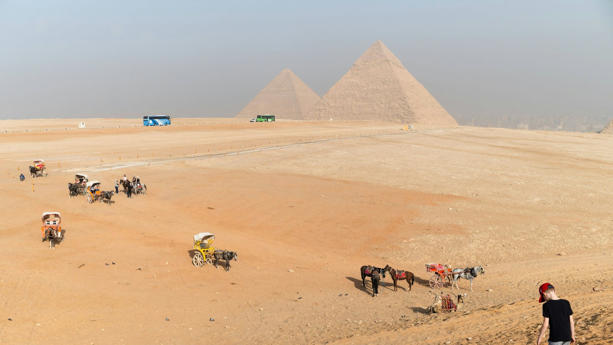 Weite Wüste mit Reitern, Kutschen und Bussen vor den ägyptischen Pyramiden von Gizeh.