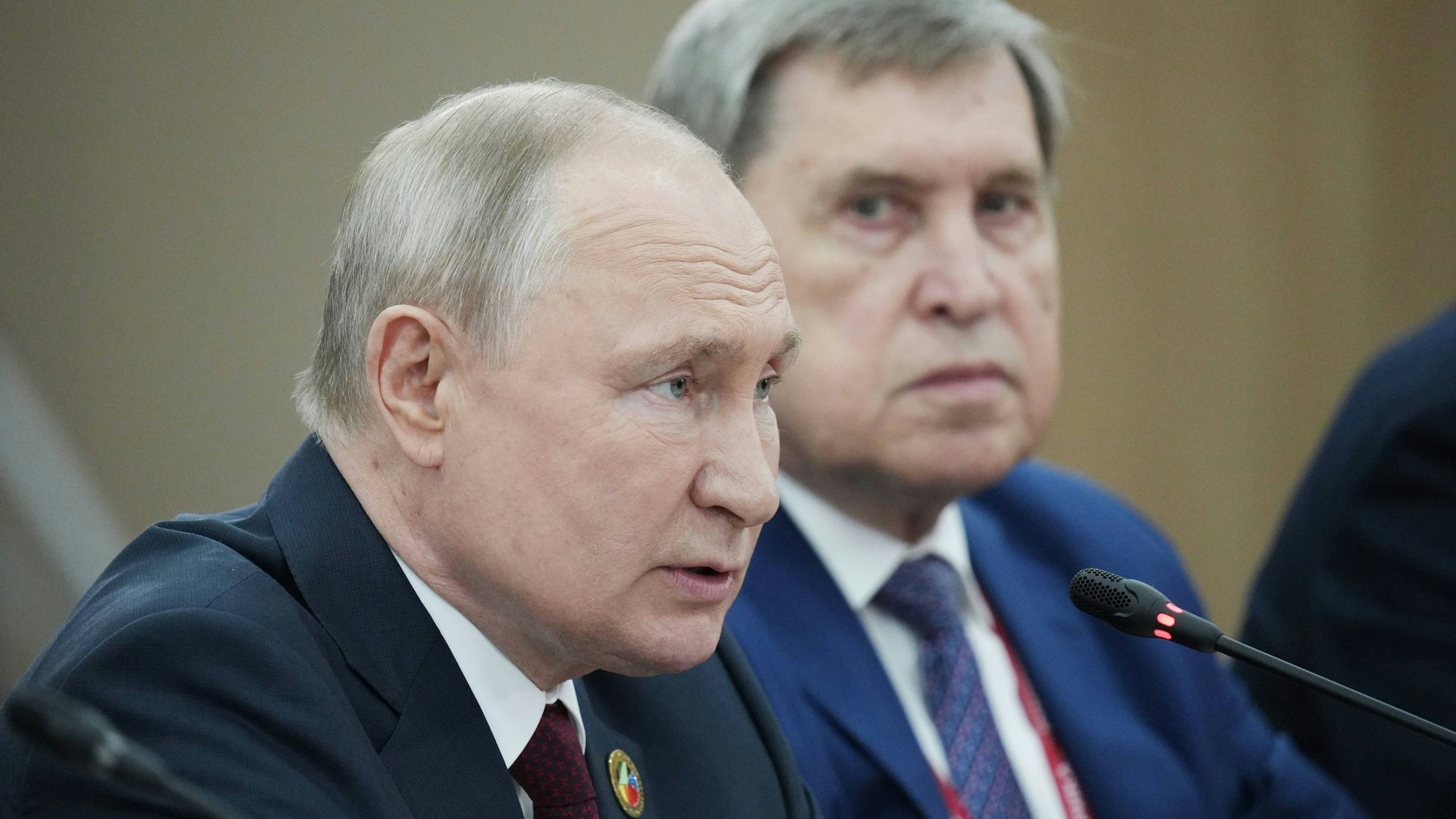 Kremlchef Wladimir Putin spricht in ein Mikrofon. Im Hintergrund ist sein hochrangiger Berater Juri Uschakow zu sehen. (Archivbild)