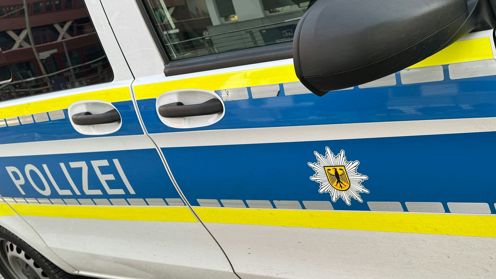Seite eines Bundespolizeifahrzeugs mit blauen Streifen, gelber Umrandung und Bundesadler-Wappen.