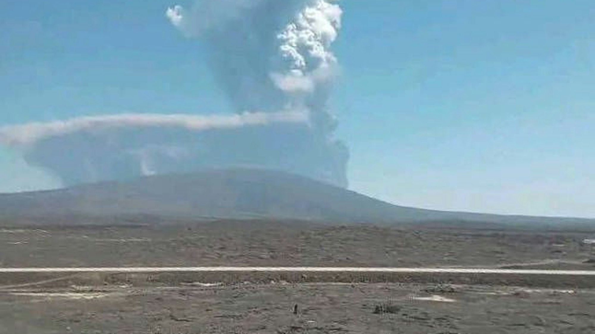 Massive Rauchsäule eines äthiopischen Vulkans über weitläufiger Lavalandschaft unter blauem Himmel