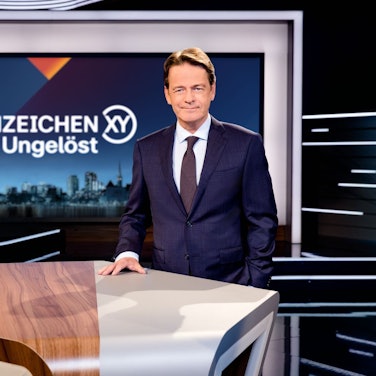 Moderator Rudi Cerne steht in der „Aktenzeichen XY ... ungelöst“-Kulisse.
