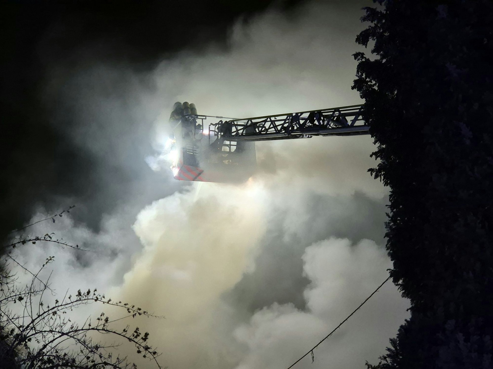 Einsatzkräfte der Feuerwehr löschen von einer Drehleiter den Brand in einem Wohnhaus.