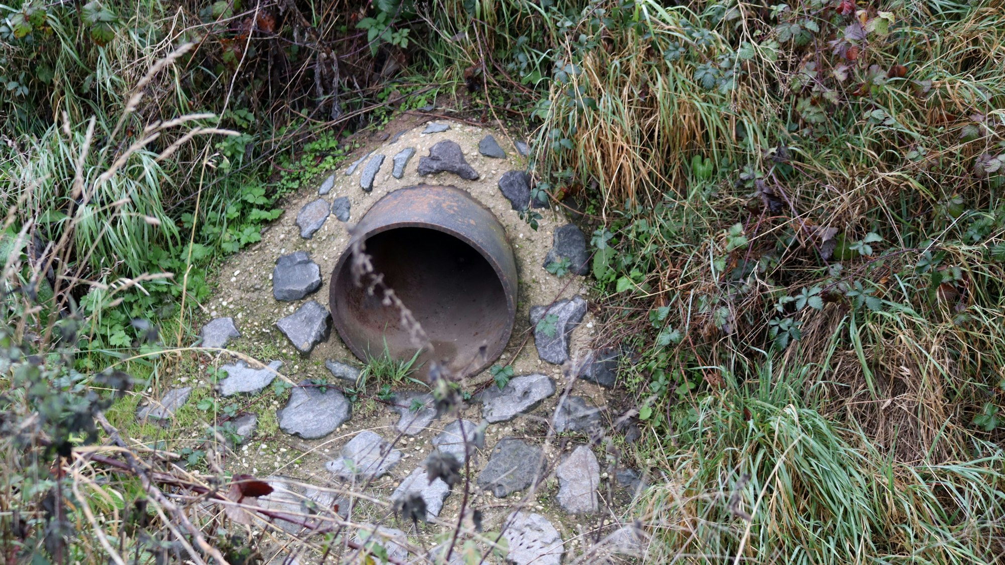Ein Durchlassrohr kommt aus einem Bahndamm. Der Bereich rund um das Rohr ist gepflastert.