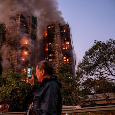 Ein Mann nimmt mit seinem Handy Rauch und Flammen auf, als ein Großbrand mehrere Wohngebäude im Wang Fuk Court in Hongkong erfasst.