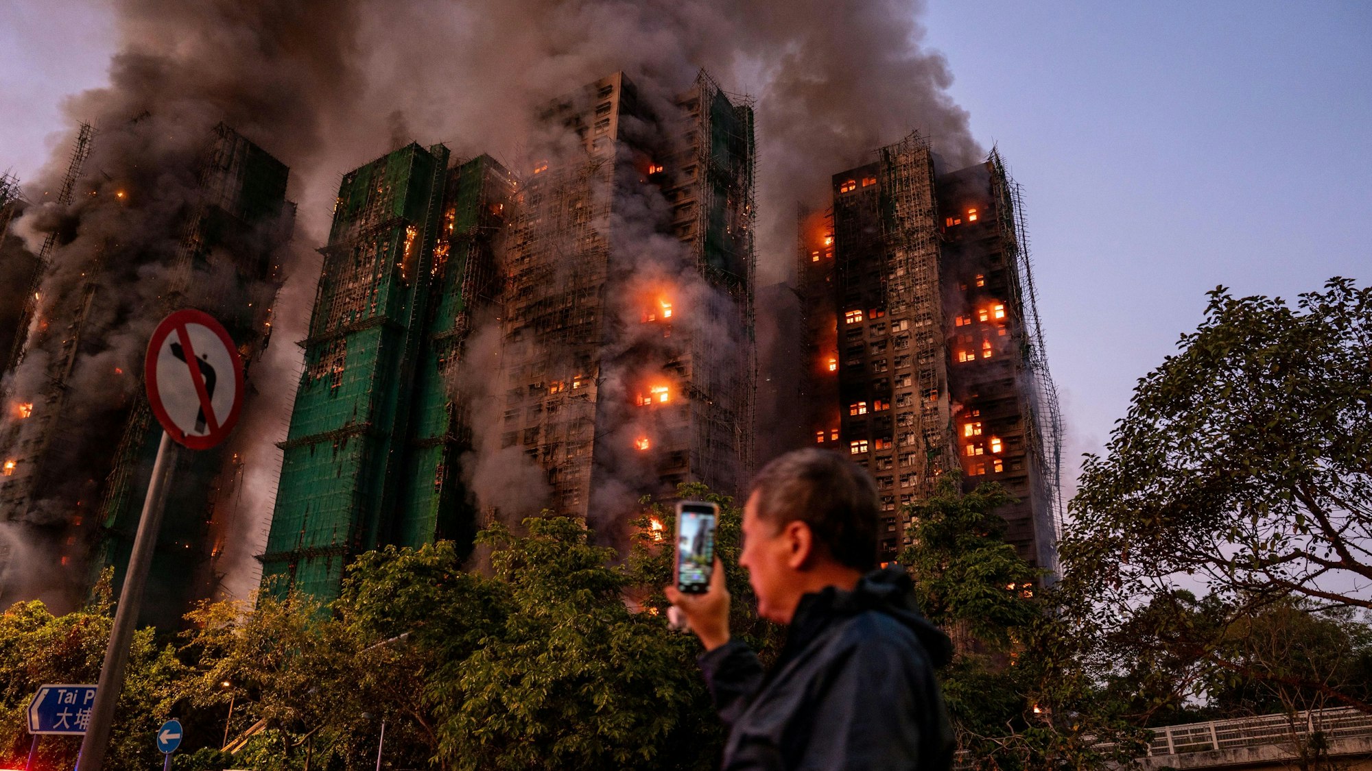 Ein Mann nimmt mit seinem Handy Rauch und Flammen auf, als ein Großbrand mehrere Wohngebäude im Wang Fuk Court in Hongkong erfasst.