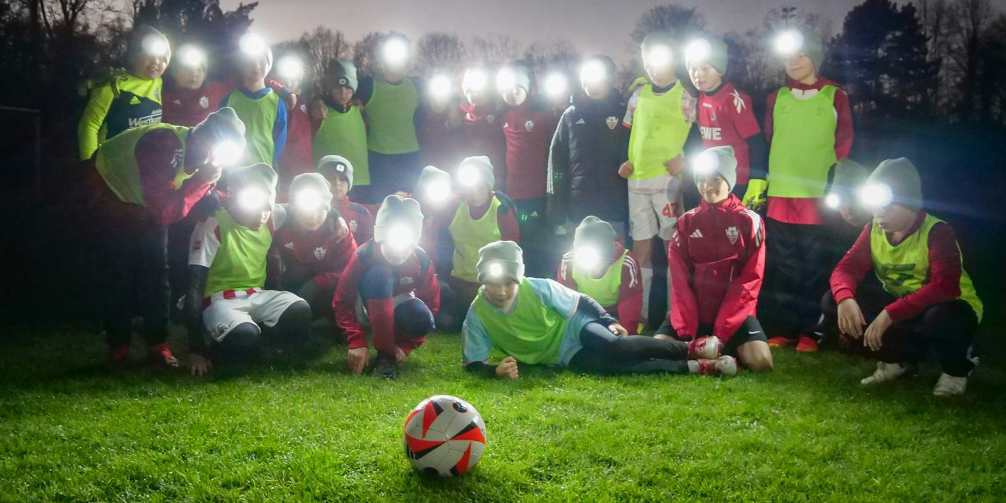 Das Bild zeigt eine Fußballmannschaft, die mit in Mützchen eingenähten Lämpchen den Ball beleuchten.