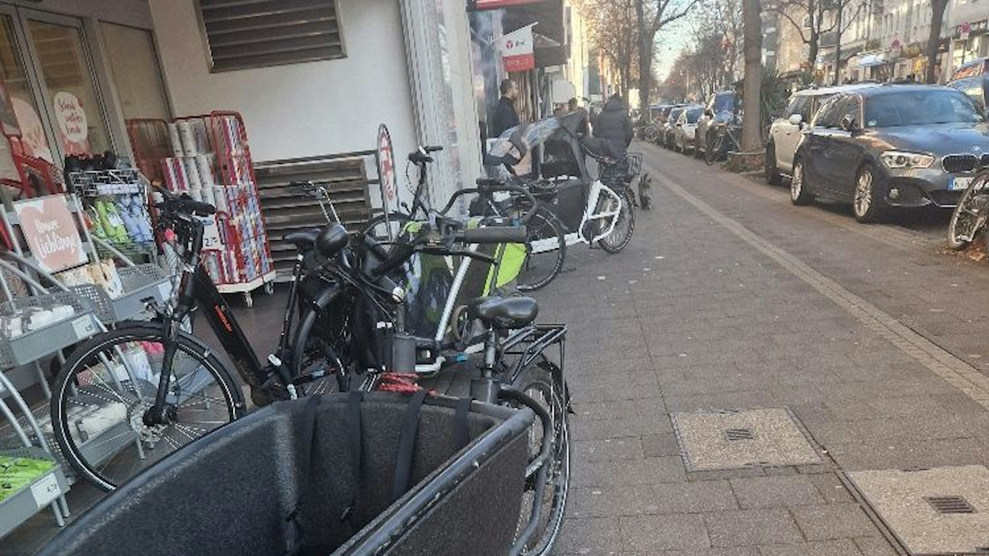Mehrere Lastenräder auf dem Bürgersteig vor einem Laden. An einem Ende ist für Fußgänger oder Kinderwagen wenig Platz.